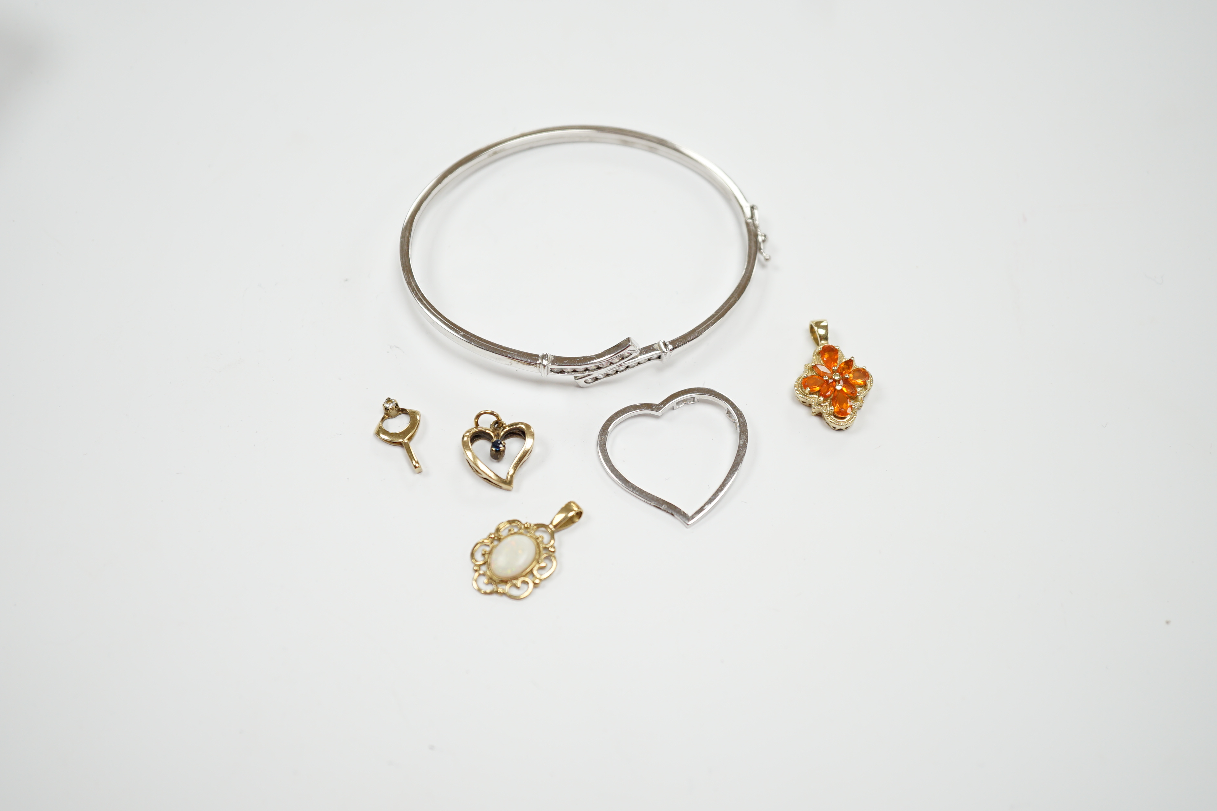 A 9ct white gold heart pendant, a 9kt bangle, two 9ct and gem set pendants and two yellow metal pendants.